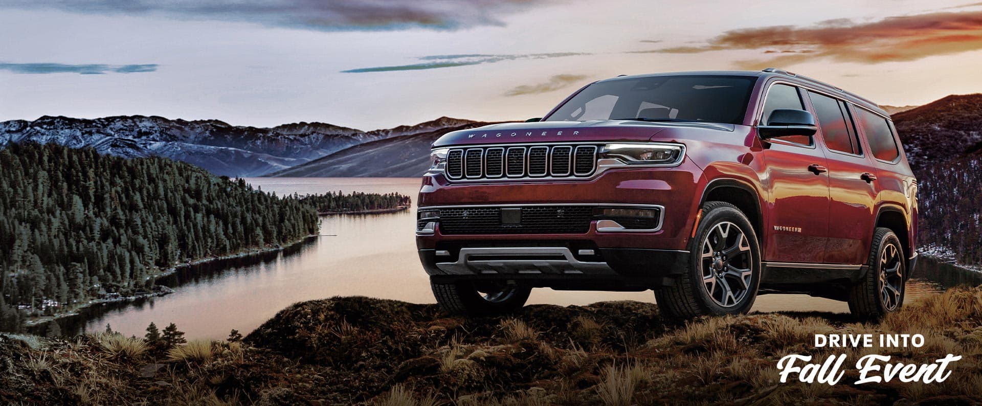 A red 2025 Jeep Wagoneer Series 3 on a grassy hill off-road, with a lake and mountains in the background. The Drive Into Fall Event.
