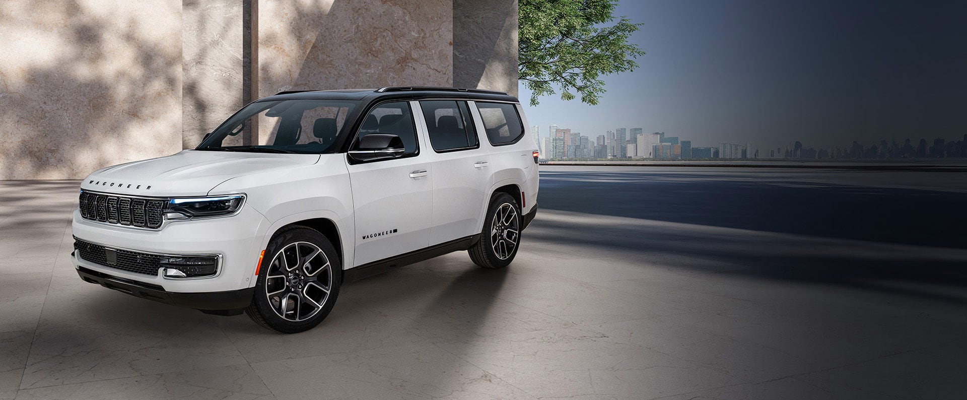 A driver-side front angle of a white 2025 Jeep Wagoneer Super with a black roof, parked in the driveway of a contemporary building.
