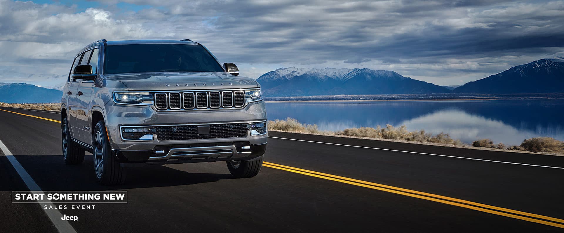 A silver 2025 Jeep Wagoneer Series 3 traveling down a highway beside a lake in winter. The Start Something New Sales Event. Jeep.