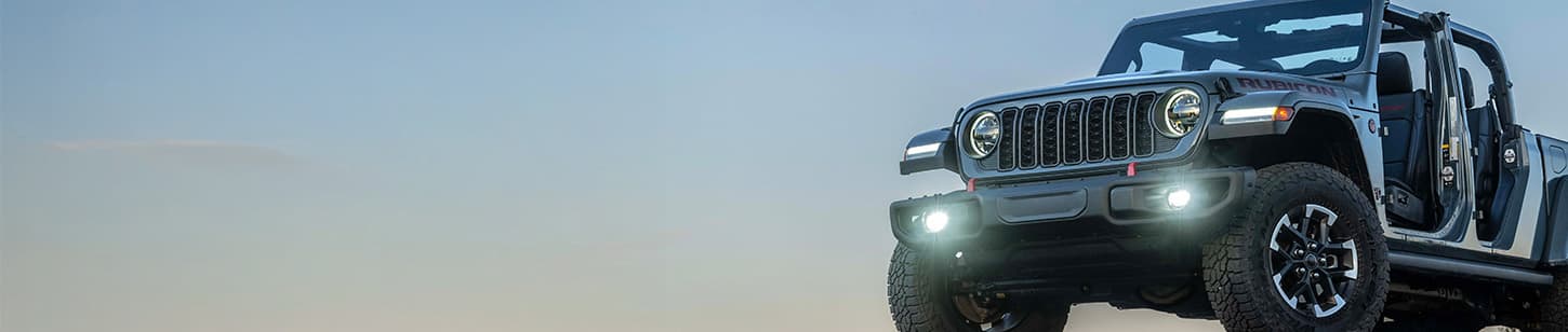 A partial driver-side front angle of a gray 2026 Jeep Gladiator Rubicon X with its doors and top removed.