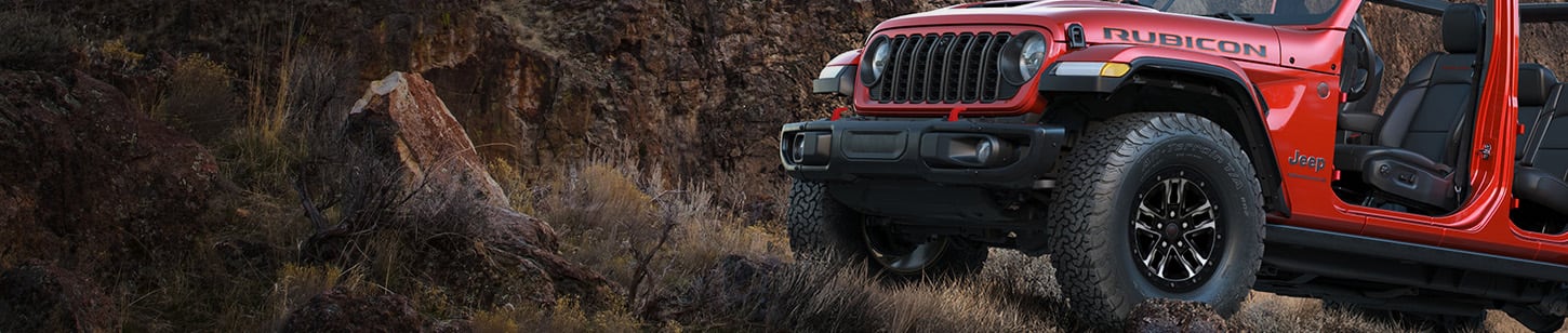 A partial driver-side front angle of a red 2026 Jeep Wrangler Rubicon X with its doors removed.