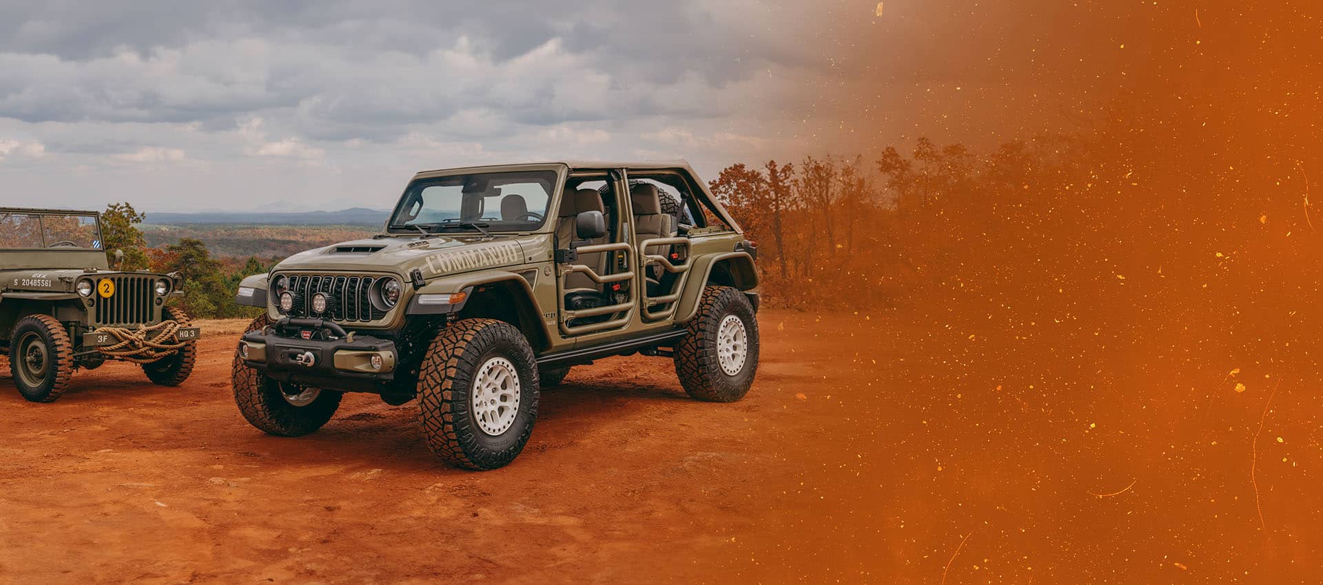 A vintage military jeep on the left and an olive drab 2026 Jeep Wrangler Commando with tube doors on the right, both parked on a clearing in the mountains. Fox Factory Vehicles.