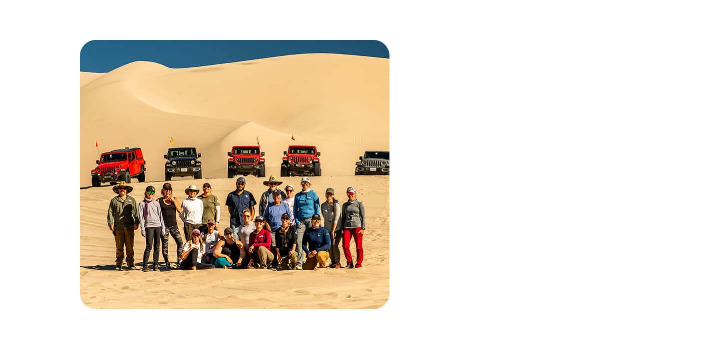 A Jeep Brand event in the desert with a group of Jeep Brand vehicle owners in the foreground and five Jeep Brand vehicles in the background.