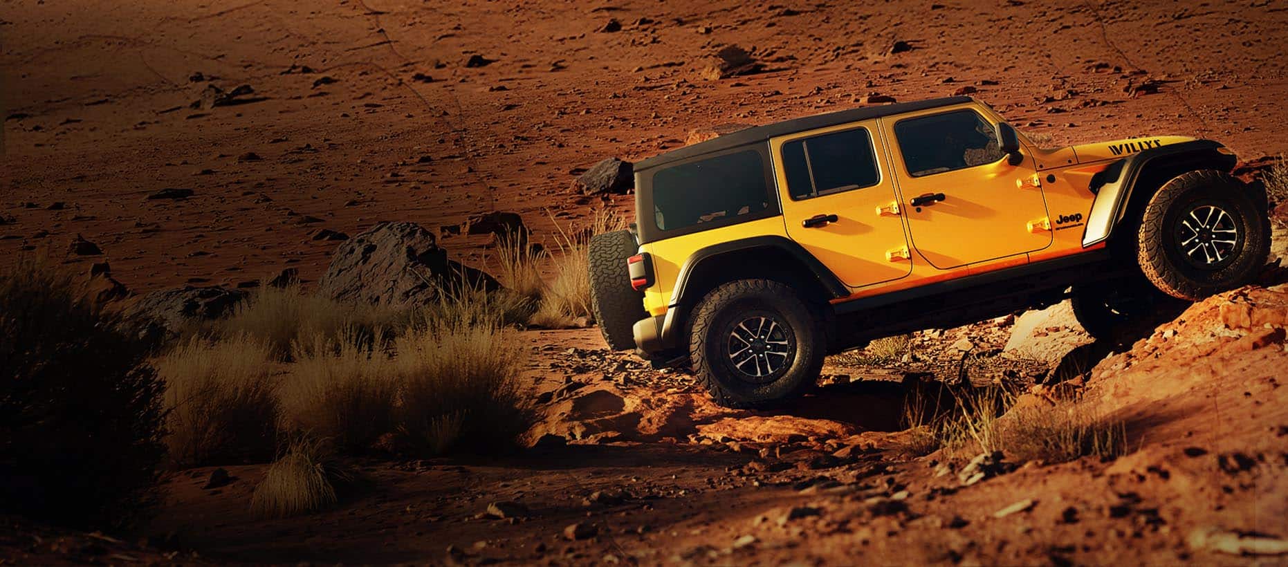 A passenger-side profile of a gold 2026 Jeep Wrangler Willys 392 crawling up a steep, rocky trail in the desert.