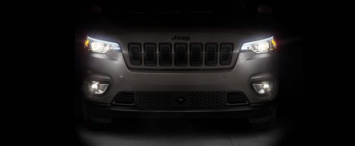 The front end of a gray 2023 Jeep Cherokee Altitude Lux with its headlamps and fog lamps lit.