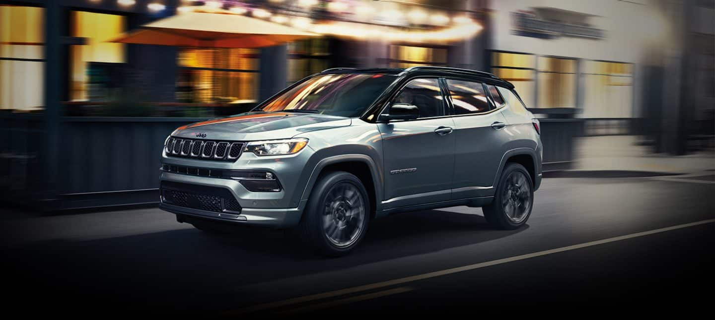 Un Jeep Compass 2024 High Altitude este condus pe o stradă din oraș pe timp de noapte, cu fundalul estompat pentru a indica faptul că vehiculul este în mișcare.