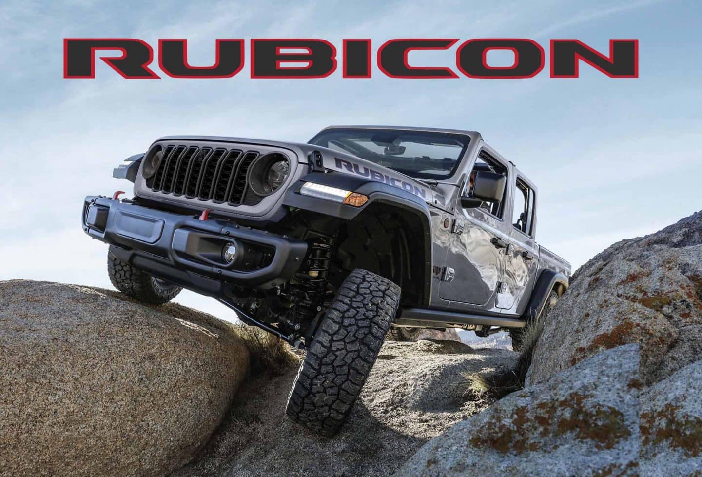 Una Jeep Gladiator Rubicon 2024 plateada con el techo desmontado, trepando por terreno rocoso, con una rueda elevada mientras pasa por una roca.