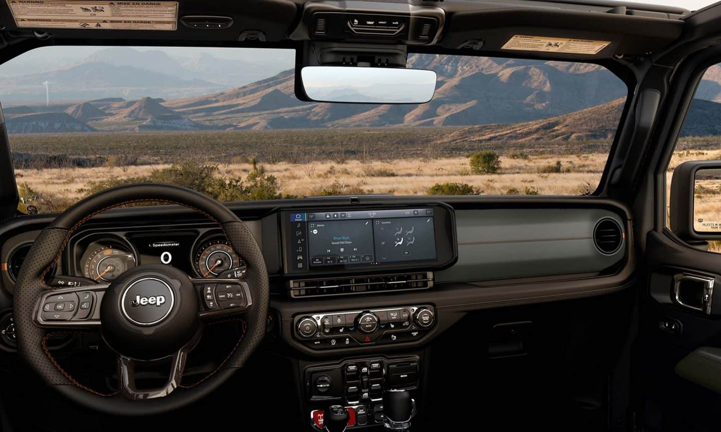 El parabrisas, el volante, la pantalla digital de información para el conductor en el panel de instrumentos y la pantalla táctil Uconnect en la Jeep Gladiator 2024.