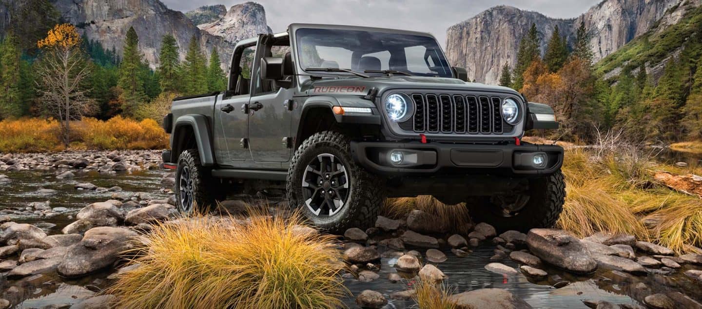 Una Jeep Gladiator Rubicon 2024 saliendo de un arroyo todoterreno con montañas de fondo.