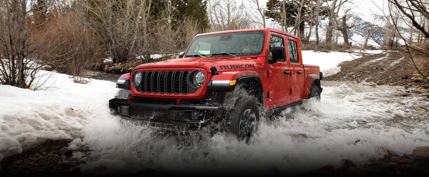 Qırmızı bir 2024 Jeep Gladiator Rubicon X, buzlu bir çaydan keçərək əraziyə uyğunlaşır. Tədbir. Gladiator.