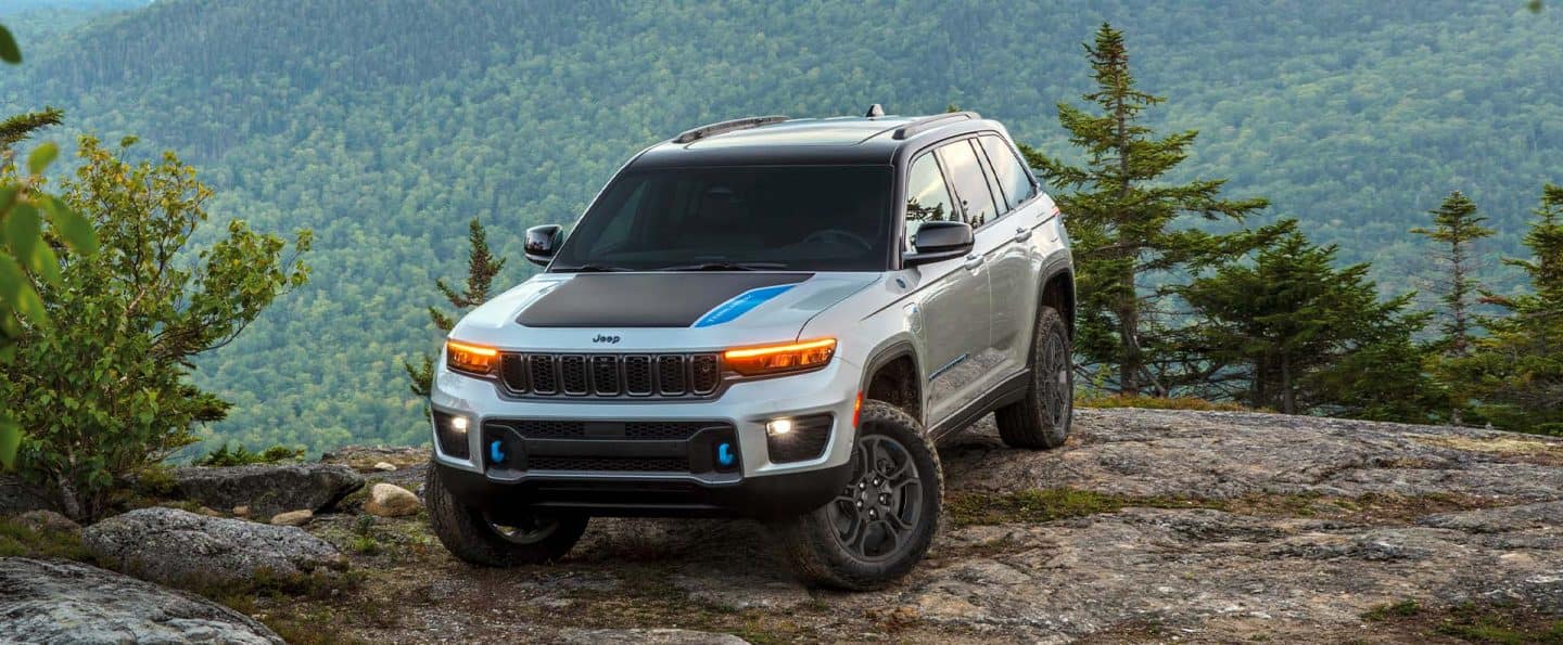 Un Jeep Grand Cherokee Trailhawk 4xe 2025 con inserción negra en el capó, estacionado en un claro en las montañas, con un bosque de fondo.