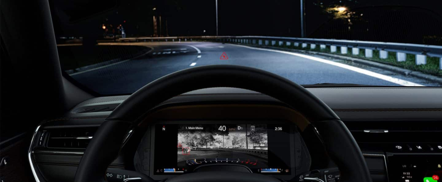 El panel de instrumentos digital del Jeep Grand Cherokee 2025, en el que se exhibe la imagen de la cámara de visión nocturna del camino por delante, que muestra un animal en la esquina izquierda de la pantalla, mientras que el animal no puede visible a través del parabrisas.