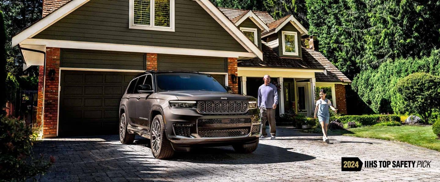 Un Jeep Grand Cherokee Summit Reserve 2025 estacionado en la entrada de una casa residencial con un padre y su hija cerca. 2024 Top Safety Pick del IIHS. 