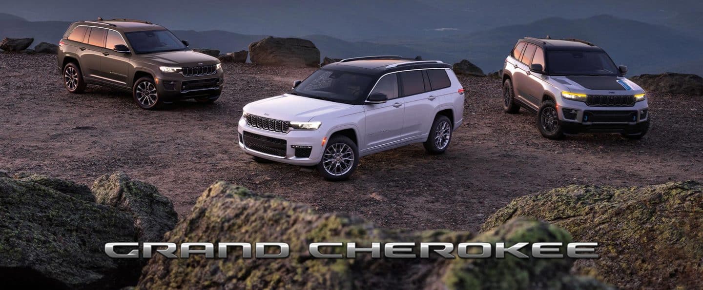 Tres modelos Grand Cherokee 2025 estacionados en un claro rocoso al anochecer, con las montañas al fondo; De izquierda a derecha: un Grand Cherokee Overland gris, un Grand Cherokee Summit blanco y un Grand Cherokee Trailhawk 4xe plateado con capó negro.