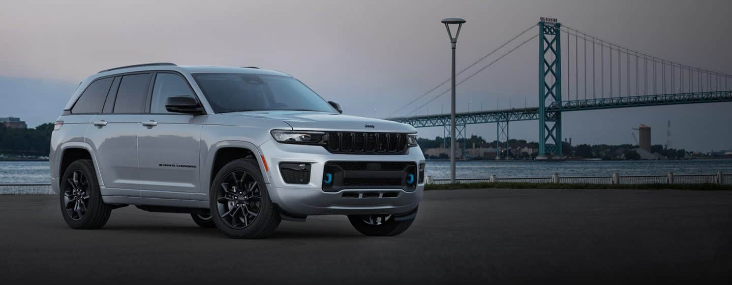 The 2023 Jeep Grand Cherokee 30th Anniversary Edition 4xe parked beside a waterway in the city at twilight with a suspension bridge in the background.