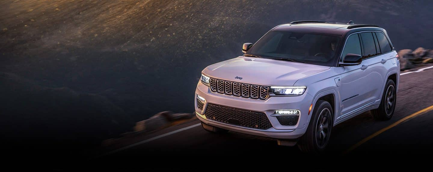 A white 2024 Jeep Grand Cherokee Trailhawk 4xe with a black hood insert, being driven off-road.