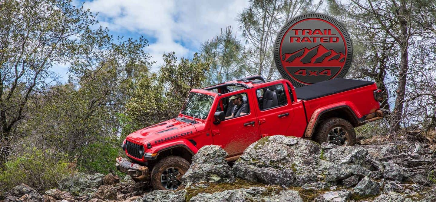 Una Jeep Gladiator Rubicon X 2025 roja sin el techo, subiendo por una serie de rocas y salientes todoterreno. El emblema Trail Rated 4x4.