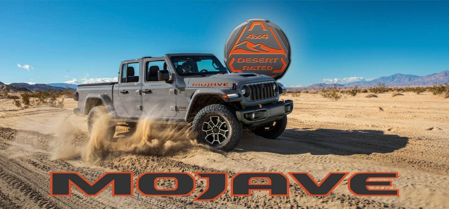 Una Jeep Gladiator Mojave X 2025 gris circulando por el desierto, echando polvo a su paso. El emblema Desert Rated 4x4. Mojave.