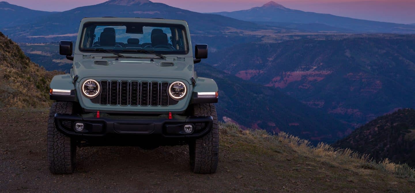 La parte delantera de un Jeep Gladiator Rubicon X 2025 azul estacionada en el borde de un acantilado con las montañas a la distancia.