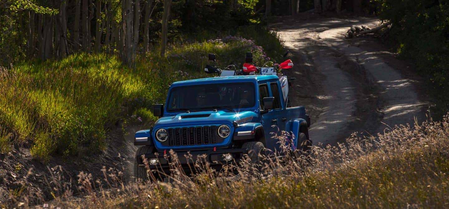 Un Jeep Gladiator Mojave X 2025 azul circulando por un sendero sinuoso con dos vehículos todoterreno en la plataforma.