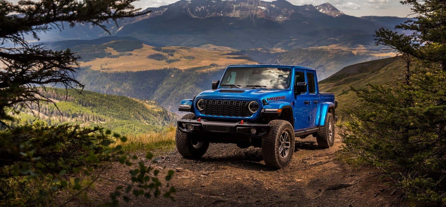 A blue 2025 Jeep Gladiator Mojave X parked on a clearing in the mountains.