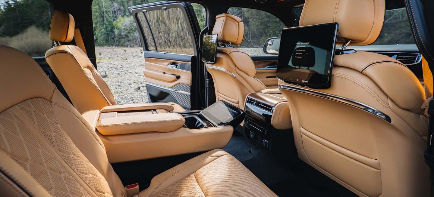 Segunda fila del Jeep Grand Wagoneer Series 3 2025 con la puerta trasera del lado del conductor abierta y el asiento central reclinado, dejando al descubierto la pantalla para la comodidad de los que viajan atrás.