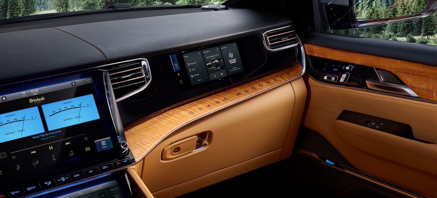 El interior del Jeep Grand Wagoneer Series 3 2025 con el foco puesto en la pantalla de confort trasero en la segunda fila y la pantalla táctil de Uconnect en la primera fila.