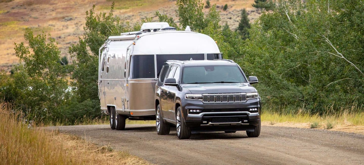 Un Jeep Grand Wagoneer Serie 3 gris del año 2025 circulando por una carretera rural, remolcando un remolque de viaje.