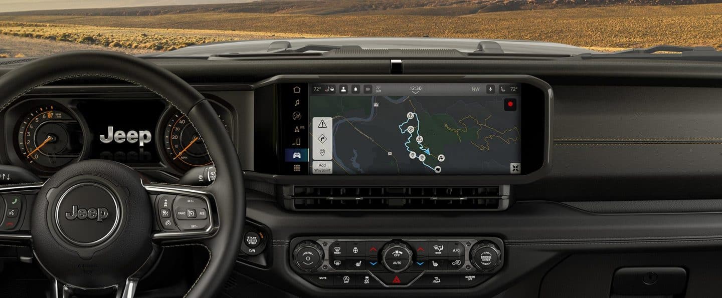 El volante, la pantalla digital en el panel de instrumentos y la pantalla táctil de Uconnect en el Jeep Wrangler 2025, en la que se muestra una de las guías de senderos todoterreno.