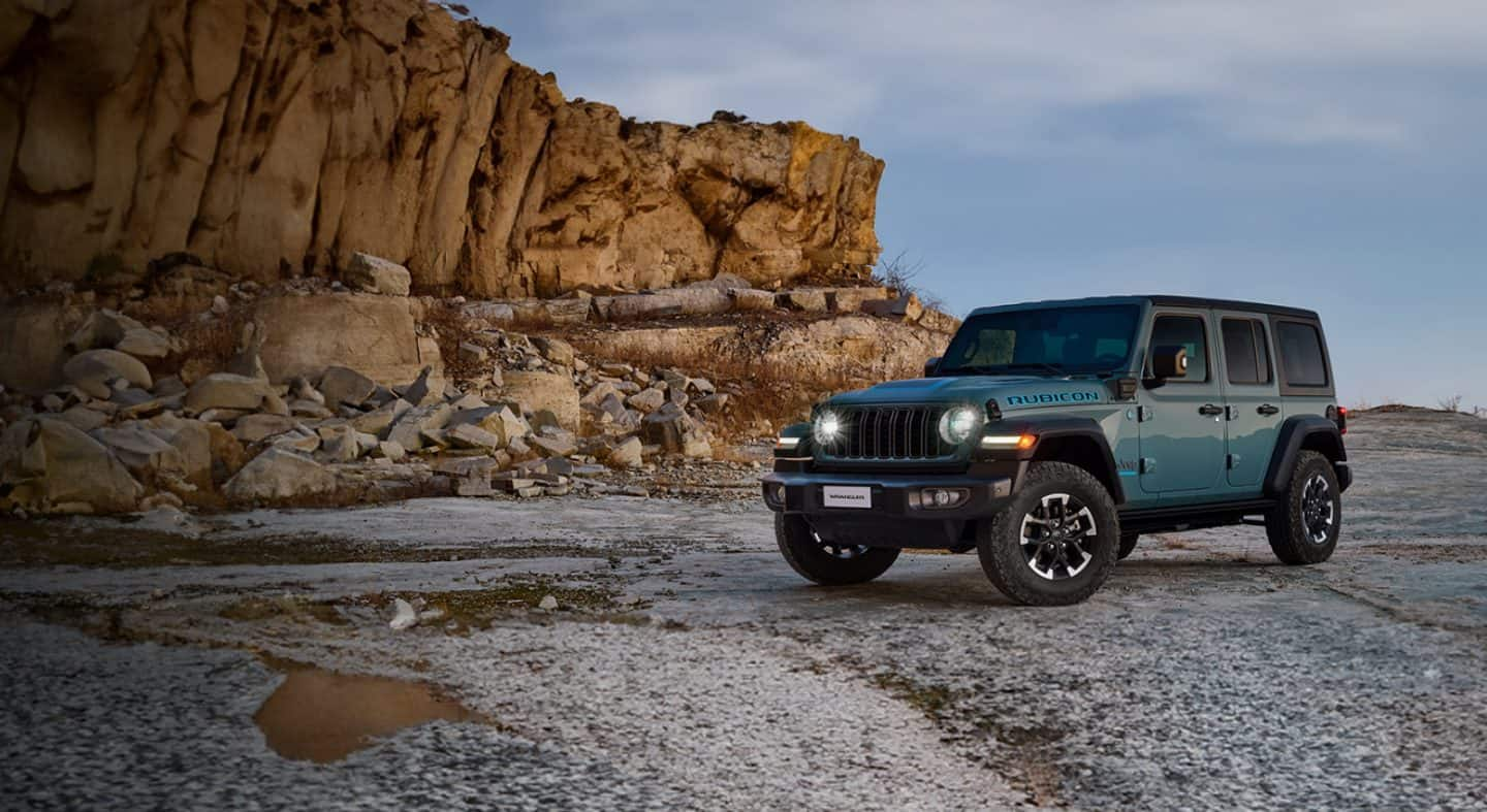 2024 m. „Jeep Wrangler Rubicon 4xe“ su nuimtomis durimis ir stogu, važiuojant smėlingu taku bekele su didžiuliais rieduliais abiejose pusėse.