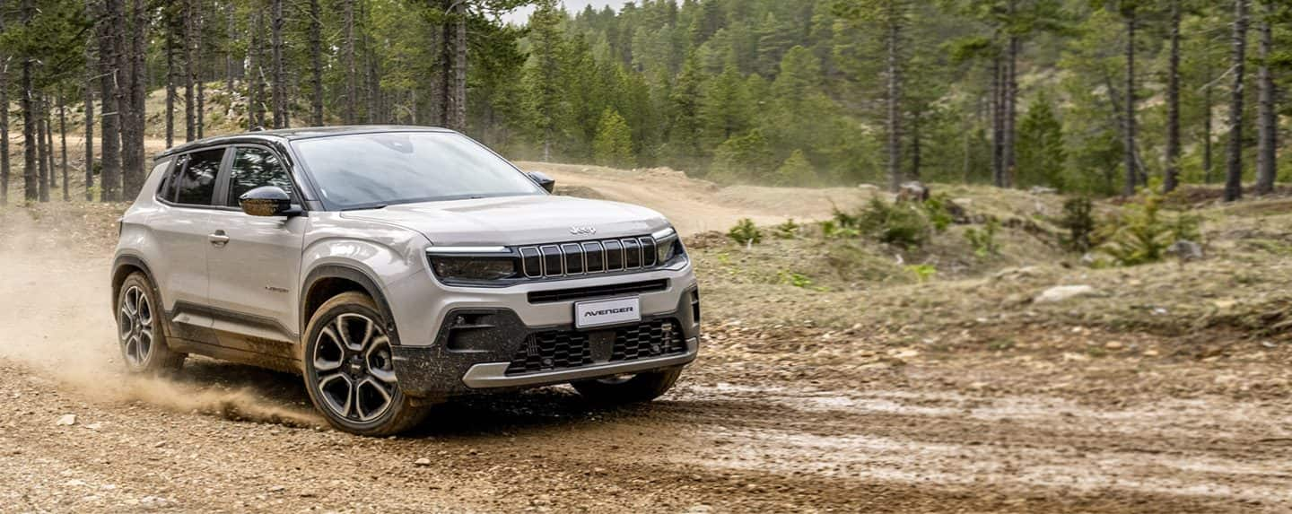 A white 2024 Jeep Grand Cherokee Trailhawk 4xe with a black hood insert, being driven off-road.