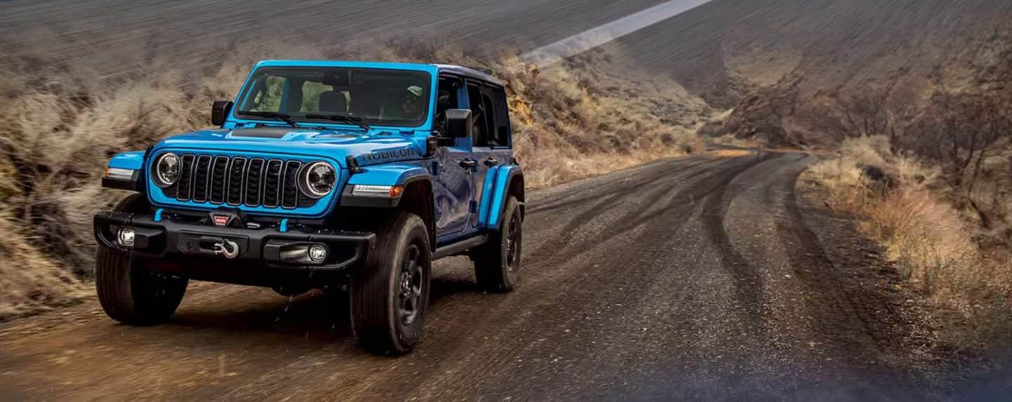 A blue 2024 Jeep Wrangler Rubicon 4xe being driven on a trail cut through the mountains.