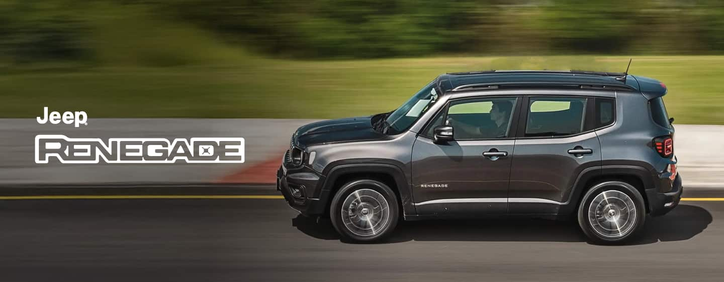 A blue gray 2023 Jeep Renegade Trailhawk fording through a narrow creek off-road, with water spraying above the vehicle's wheel wells. Renegade.