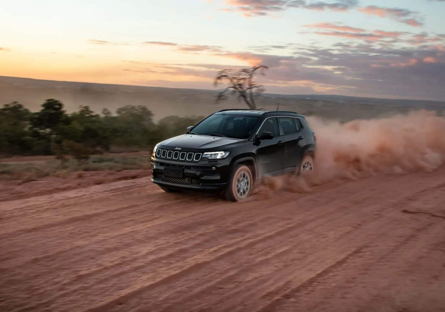 A 2023 Jeep Compass High Altitude being driven through an intersection on a city street. A large neon checkmark is superimposed over the background.