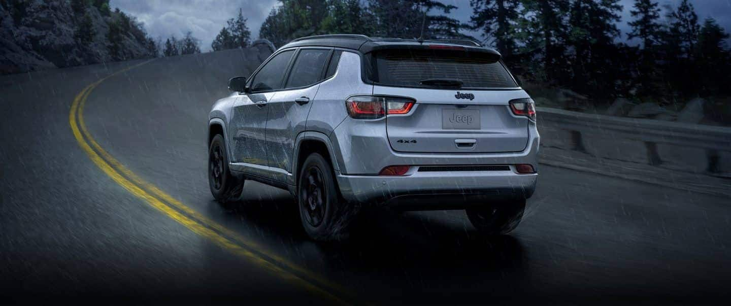 A rear view of a 2023 Jeep Compass High Altitude being driven on a winding highway during a rainstorm.