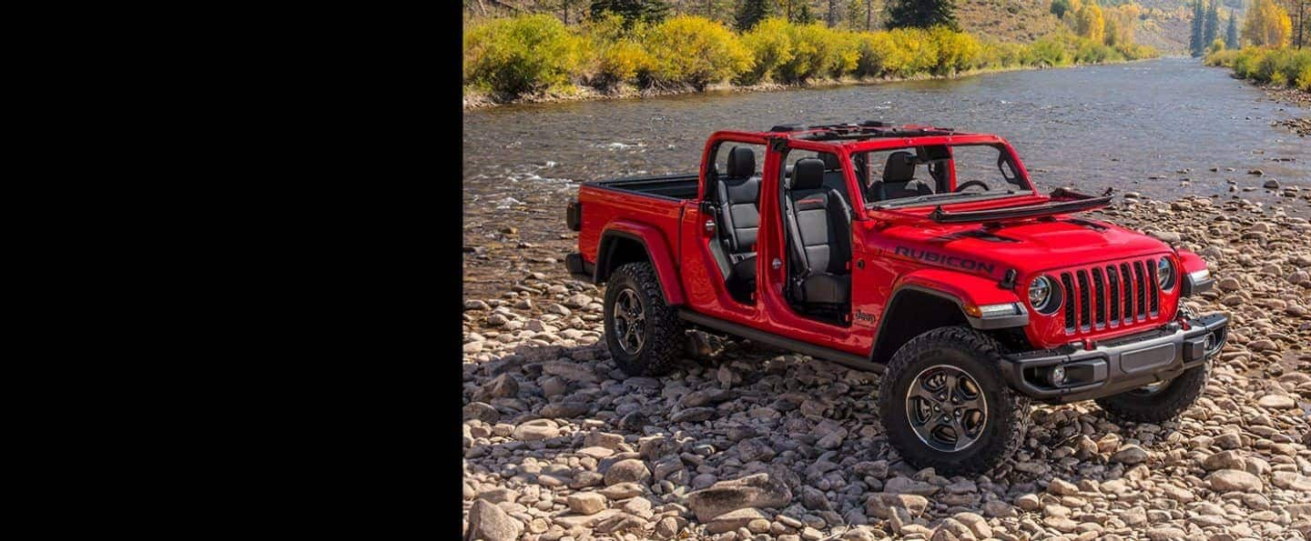 The 2023 Jeep Gladiator Rubicon with its top and doors off, parked on a pebbled riverbank.