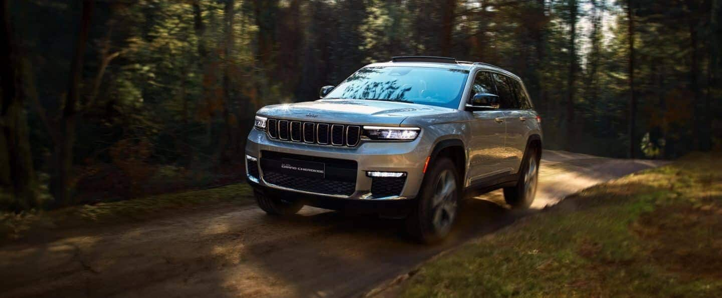 Una fila de cuatro modelos Jeep Grand Cherokee estacionados en un claro con montañas nevadas al fondo. De izquierda a derecha: un Grand Cherokee Summit rojo, un Grand Cherokee Summit Reserve 4xe blanco, un Grand Cherokee Trailhawk 4xe negro y un Grand Cherokee Limited azul. El logotipo del evento de ventas del Día de los Caídos.