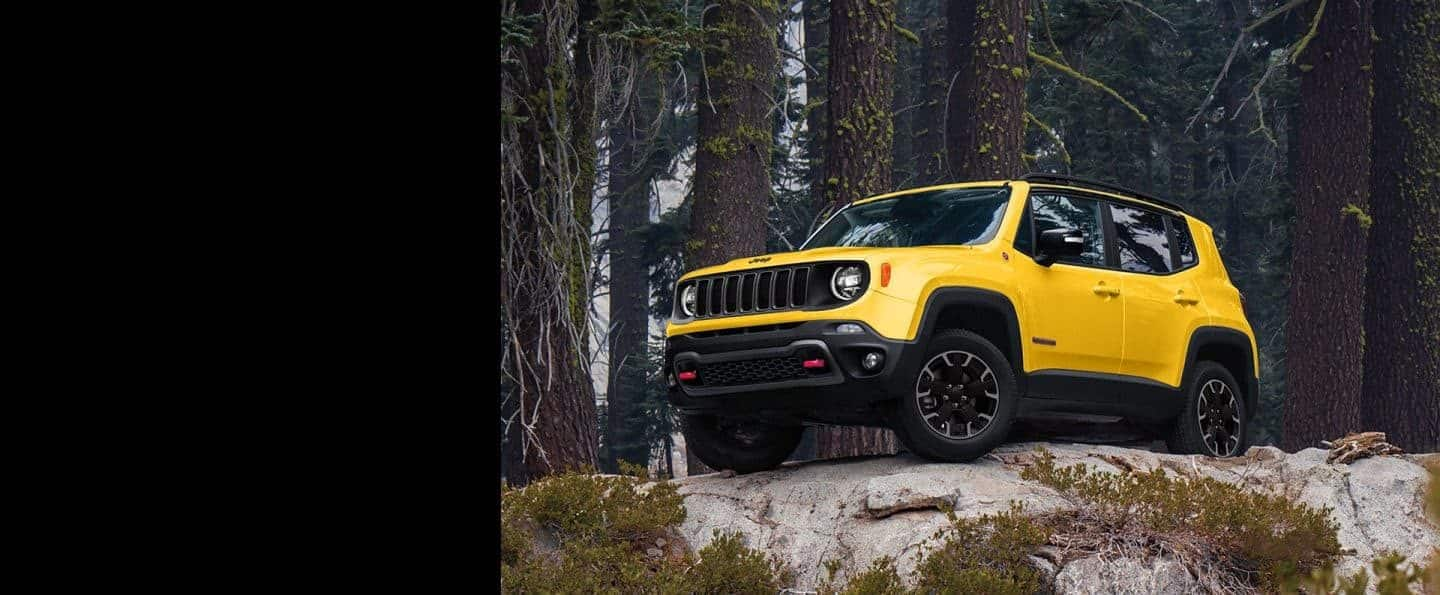 A yellow 2023 Jeep Renegade Trailhawk parked on a rocky outcrop in the woods.