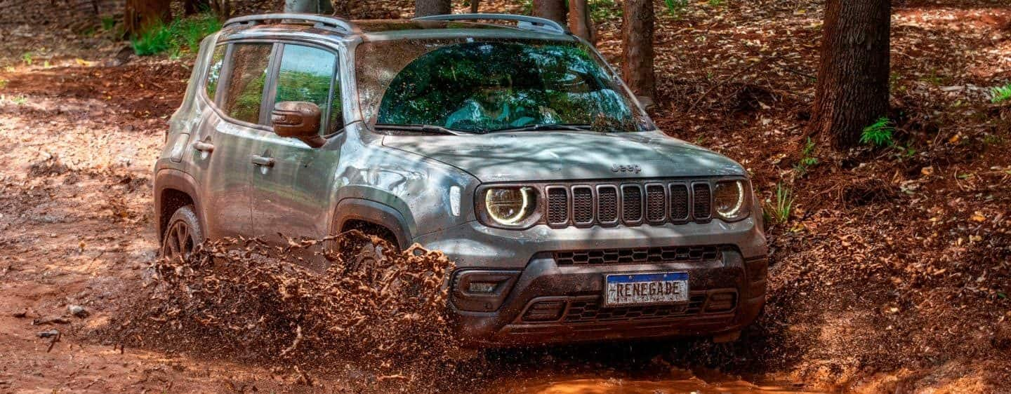 A yellow 2023 Jeep Renegade Trailhawk parked on bare rock with trees in the background.