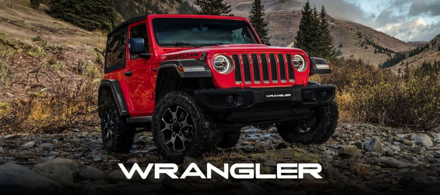 A 2024 Jeep Wrangler Rubicon 4xe with its doors and roof removed, being driven on a sandy trail off-road, with huge boulders on both sides.