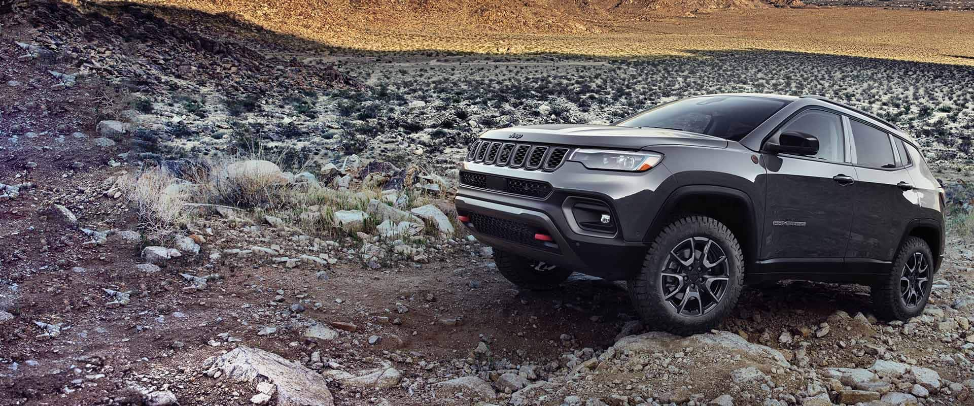 A gray 2024 Jeep Compass Trailhawk crawling over large and small rocks and stones off-road.