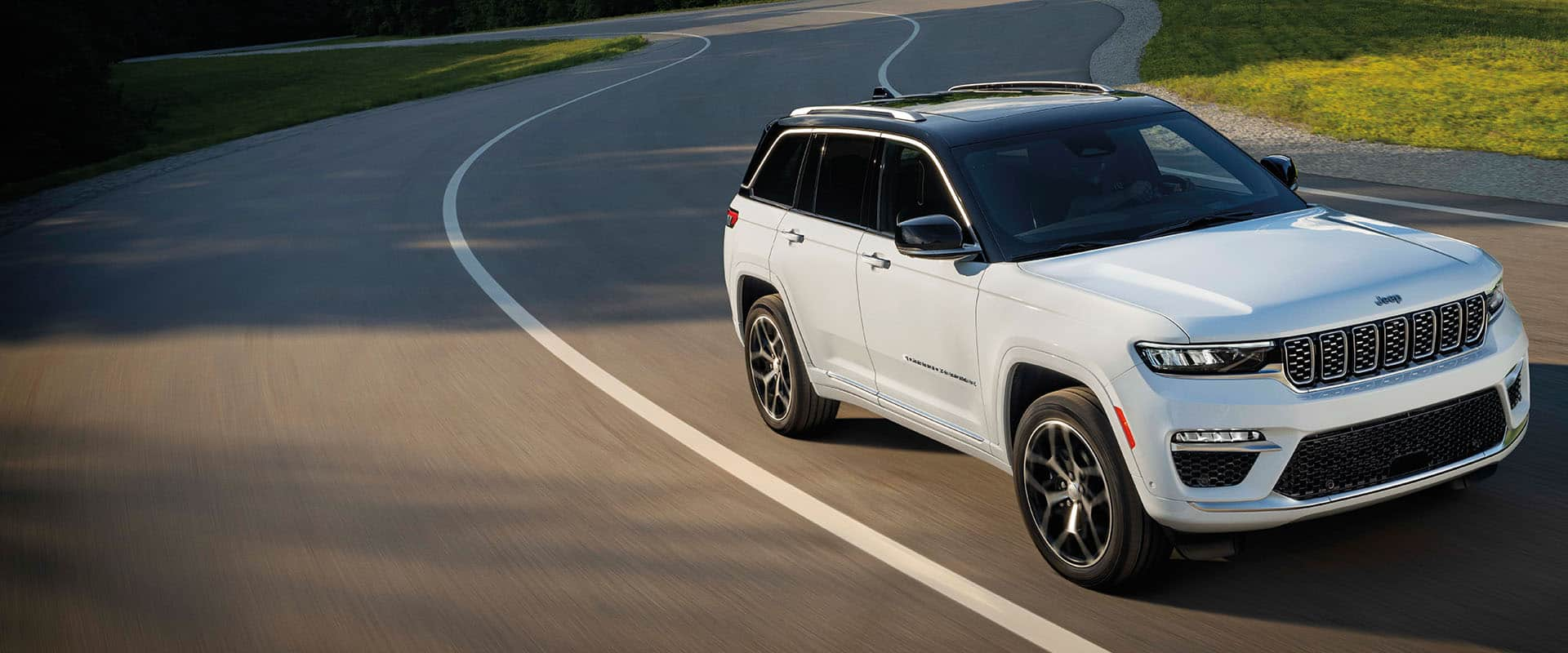 A white 2024 Jeep Grand Cherokee Summit Reserve being driven on a curved highway.