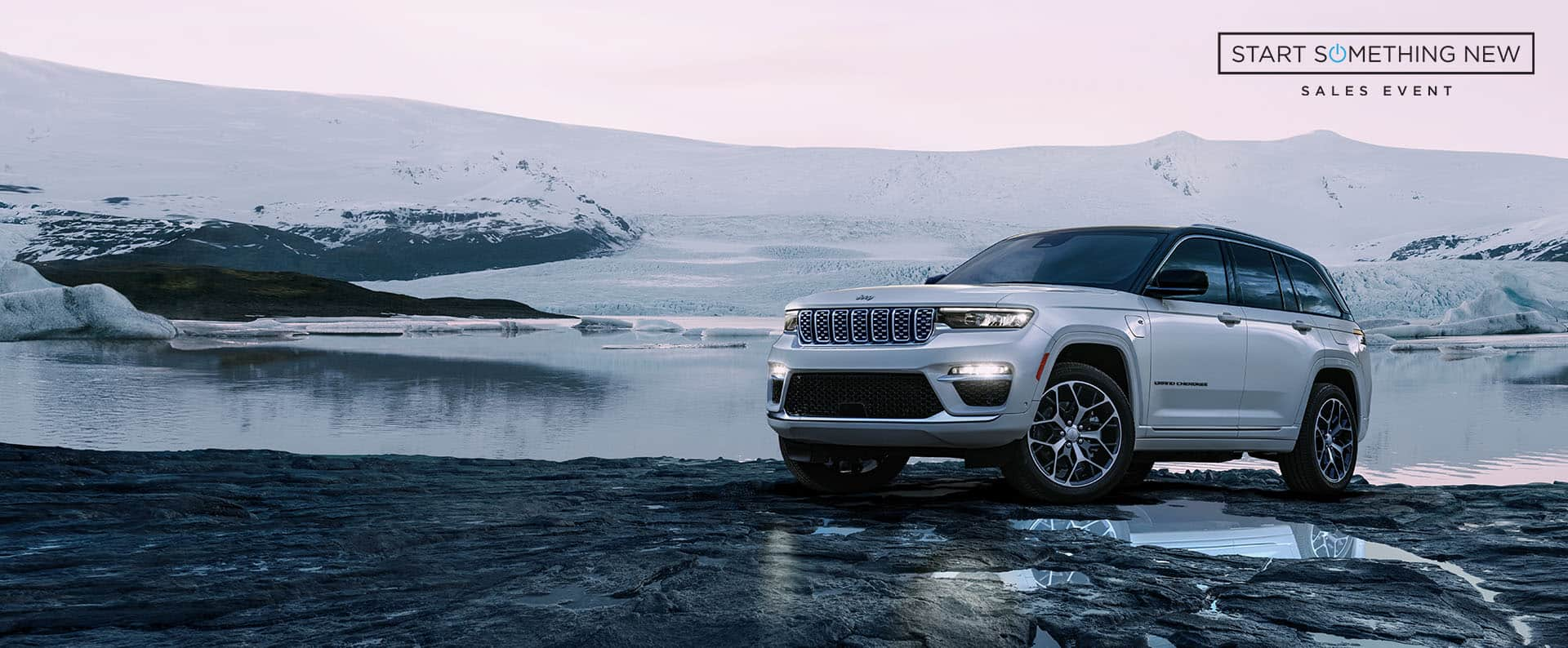 A white 2024 Jeep Grand Cherokee Summit Reserve 4xe parked on a trail off-road, with snow-covered hills in the background. Start Something New Sales Event logo.