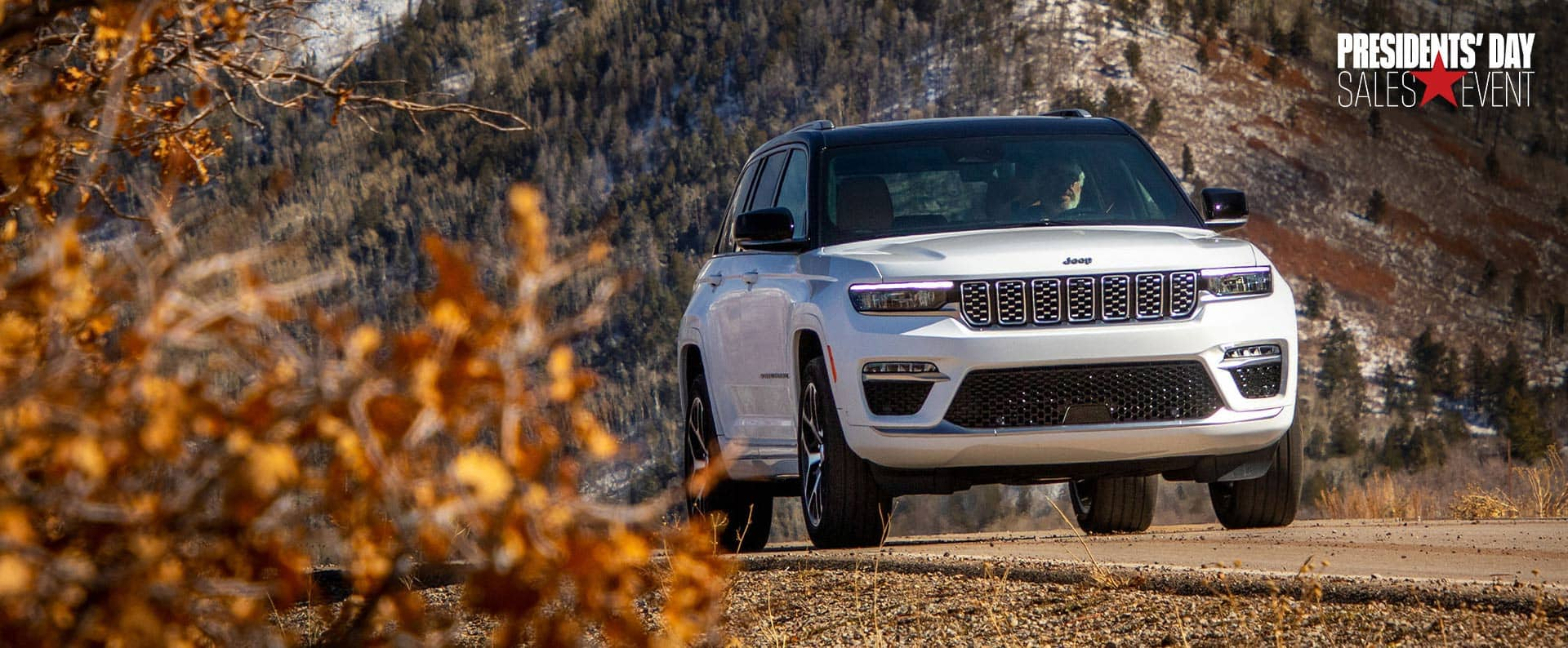 A white 2024 Jeep Grand Cherokee Summit Reserve 4xe parked on a trail off-road, with snow-covered hills in the background. President's day Event.