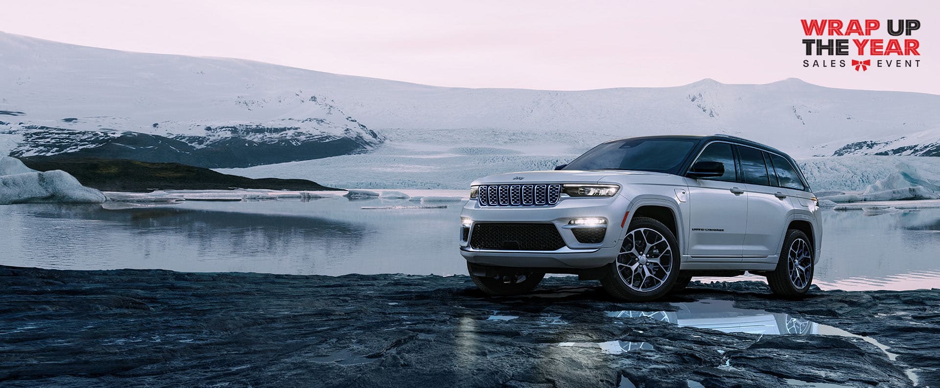 Un Jeep Grand Cherokee Summit Reserve 4xe 2024 blanco estacionado en un sendero fuera de la carretera, con colinas cubiertas de nieve de fondo. Evento de ventas Fin de año.