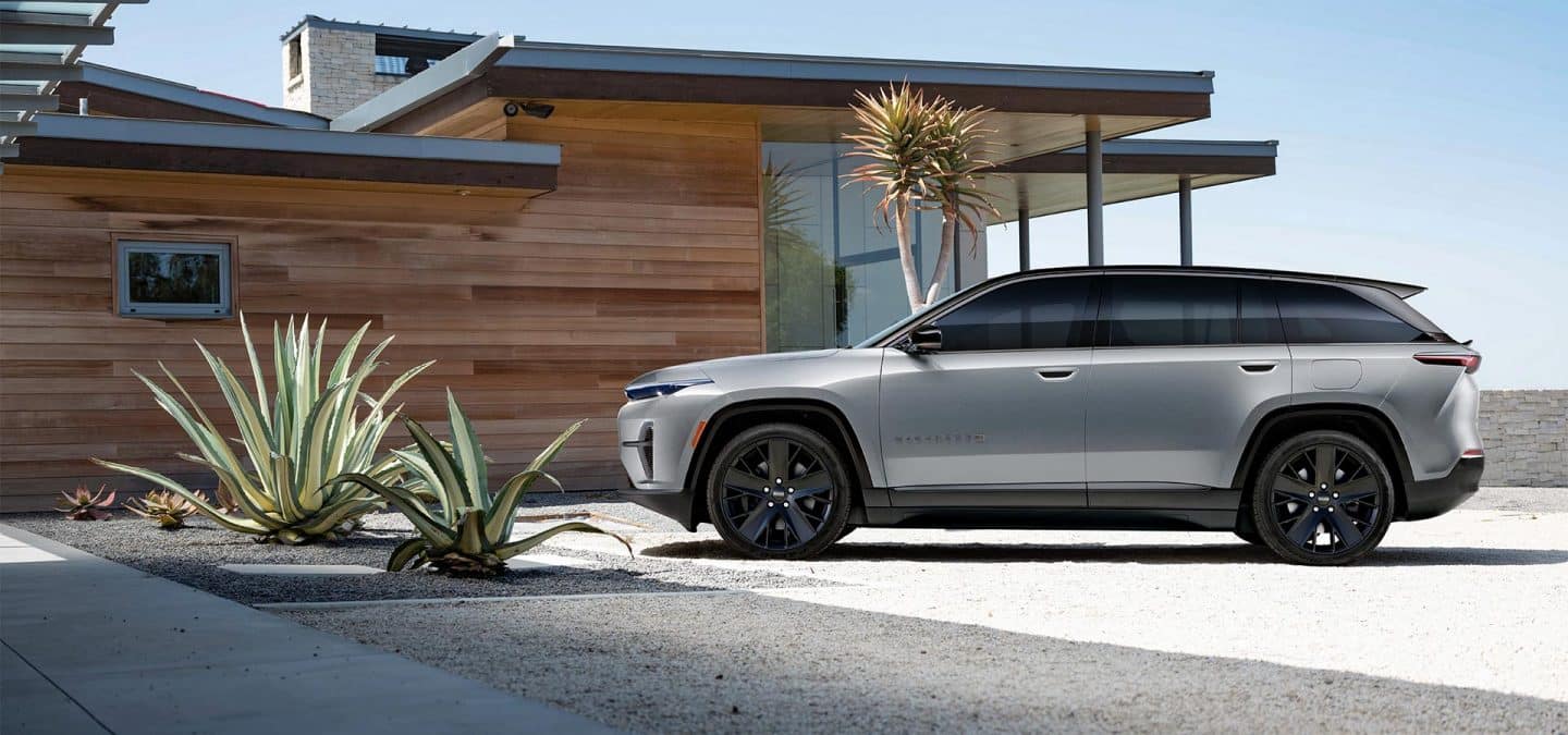 Display A driver-side profile of a silver 2024 Jeep Wagoneer S Launch Edition parked beside a contemporary beachfront home.