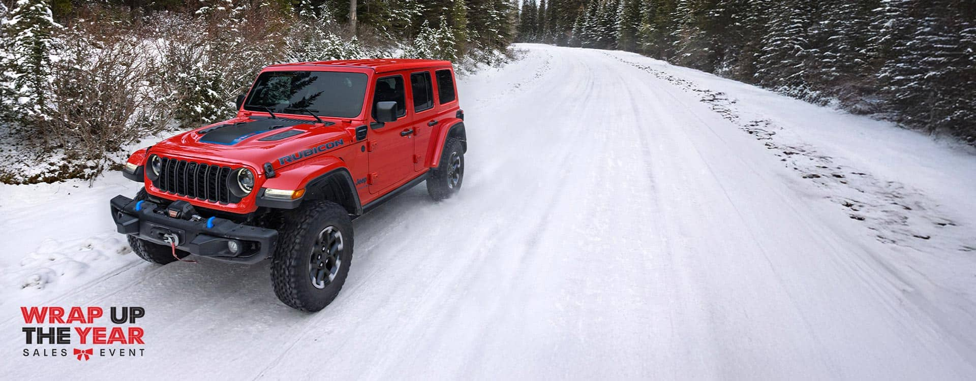 A red 2024 Jeep Wrangler Rubicon X 4xe traveling on a snow-covered road in a forest. Wrap Up The Year Sales Event.