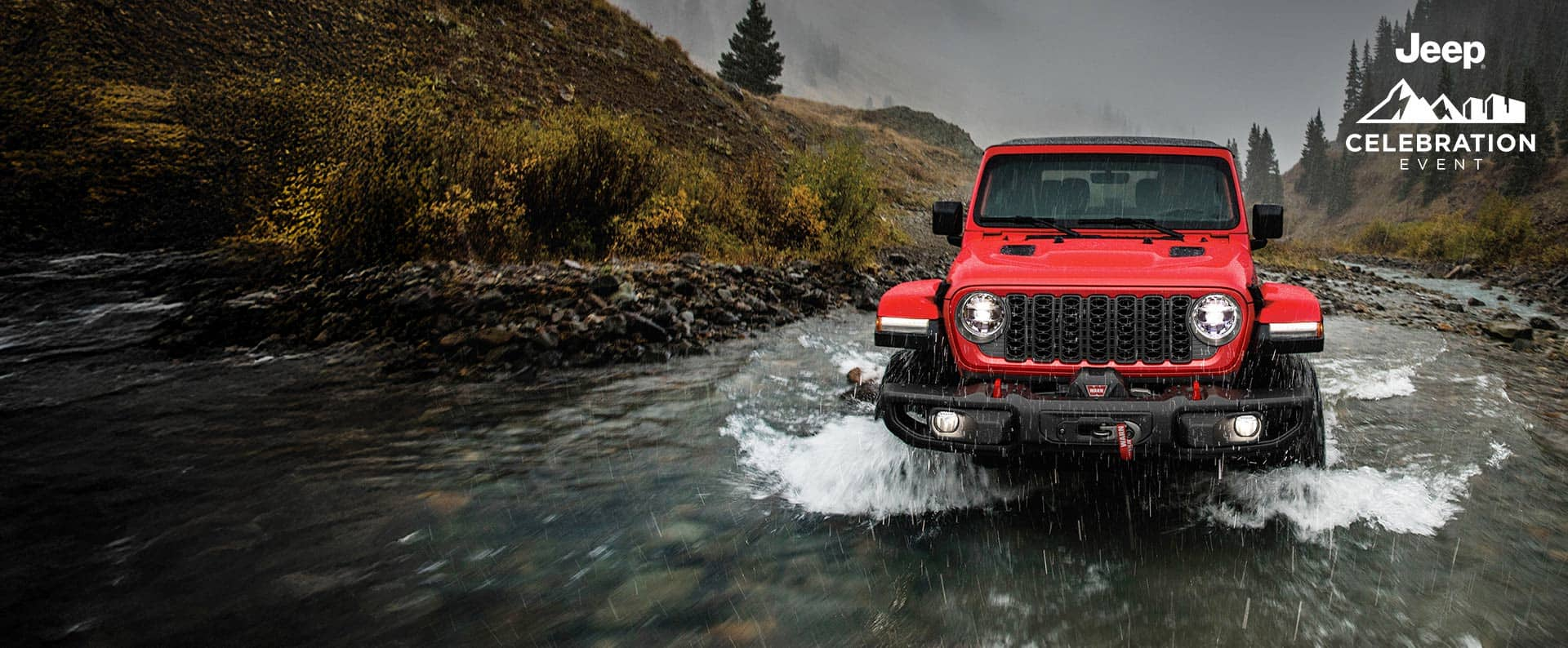 A front angle of a red 2024 Jeep Wrangler Rubicon being driven through a stream, following its path. Jeep Celebration Event.