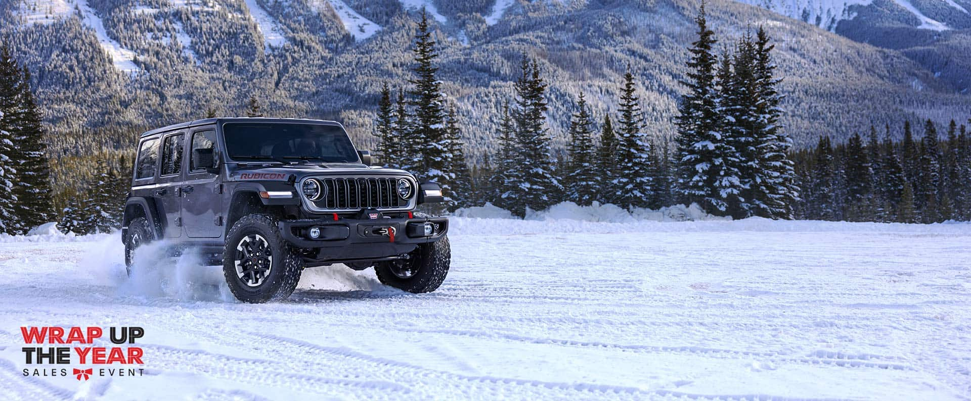 Un Jeep Wrangler Rubicon 2024 gris circulando por un sendero cubierto de nieve en un bosque. Logo de Evento de ventas de Fin de año.