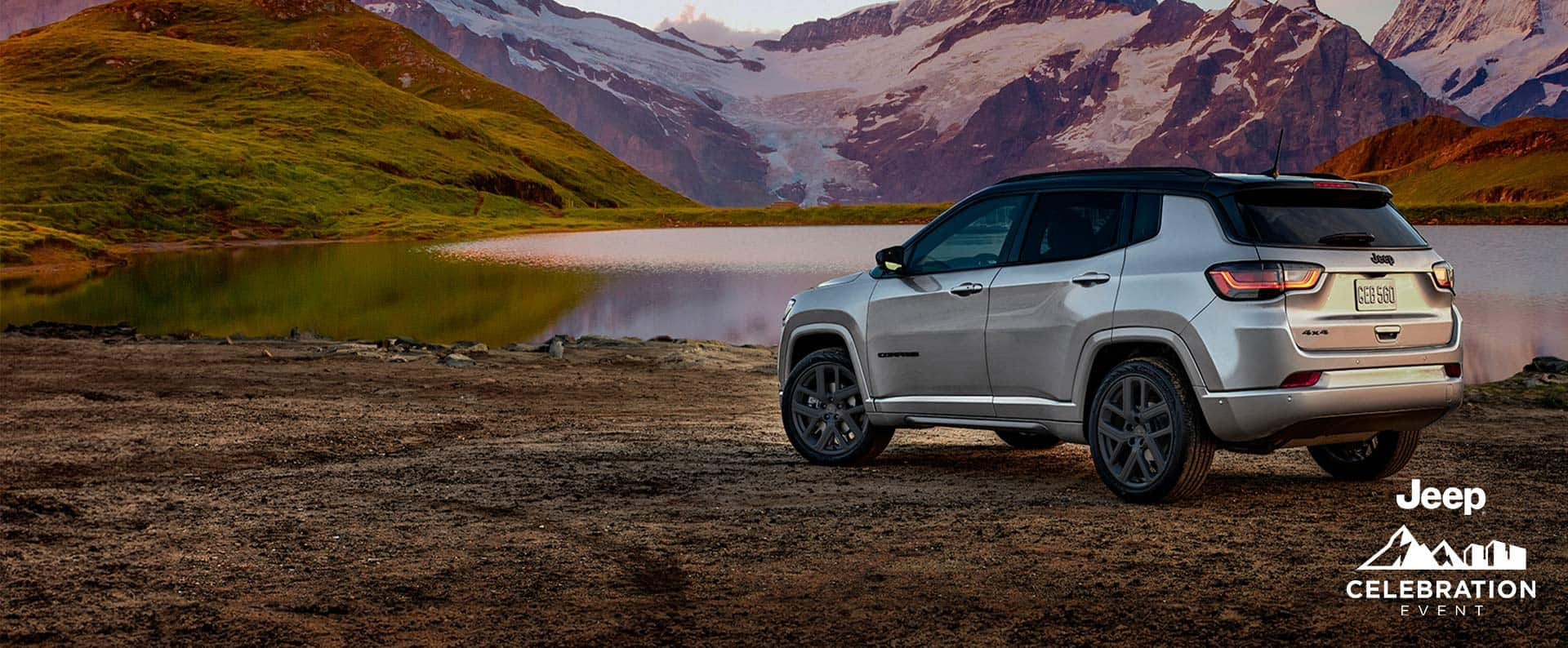 A silver 2025 Jeep Compass Limited with the High Altitude Package, parked beside a mountain lake at sunset. Jeep Celebration Event.